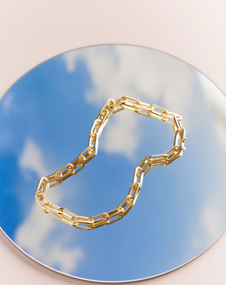 Styled product photography for the Roma Chain on a mirror with a sky reflection.